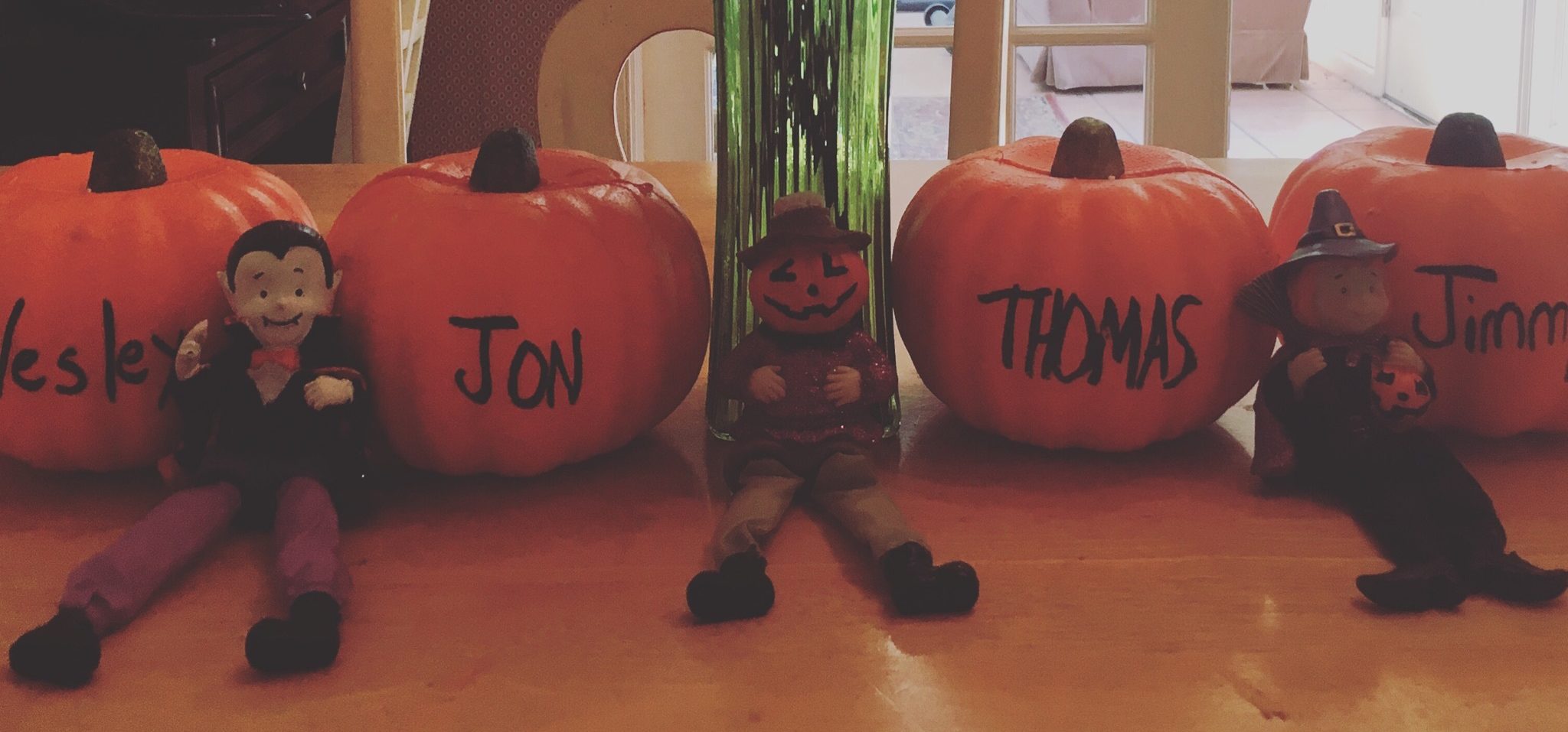 Four pumpkins, each with a person's name written on it, on a counter in a home.